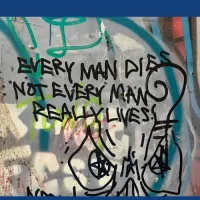 A heavily graffitied wall can be seen. Colours in the background are grey, with blue lines and faded white letters, in the foreground on the wall in black spray paint are the words: EVERY MAN DIES NOT EVERY MAN REALLY LIVES. 