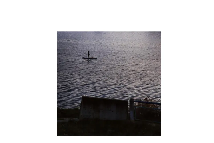 The photo shows a stand-up paddleboarder on the enormous Danube river in the cold of November. They appear small, vulnerable, isolated, and exposed. While the river itself is not inherently hostile, its scale, the cold season, and the absence of other people create a sense of precariousness.